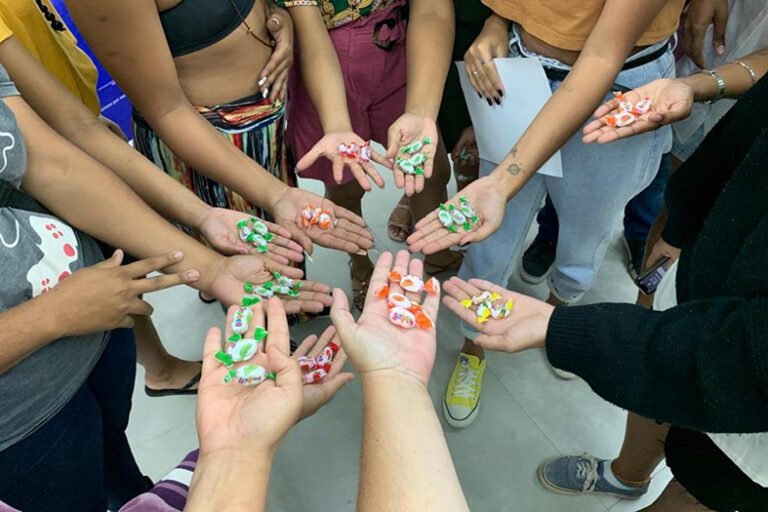 Pessoas com braços estendidos formam um círculo com as palmas das mãos mostrando doces. 