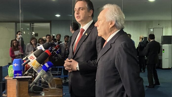 Rodrigo Pacheco e Ricardo Lewandoski, ambos de terno, em frente ao púlpito de entrevistas do Senado